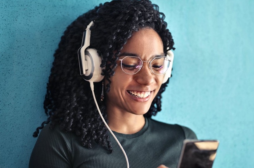 Girl smiling wearing headphones and looking down at her phone