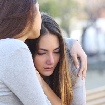 2 girls outside hugging, one crying while leaning into the other