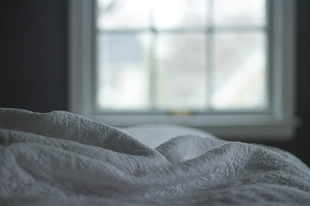 Rumpled blanket on a bed in front of a window