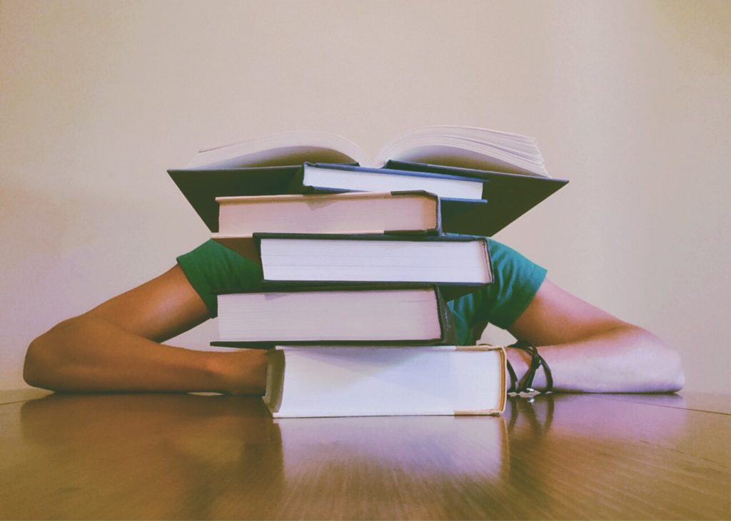 Stack of books with a person behind it with their head down and elbows bent out